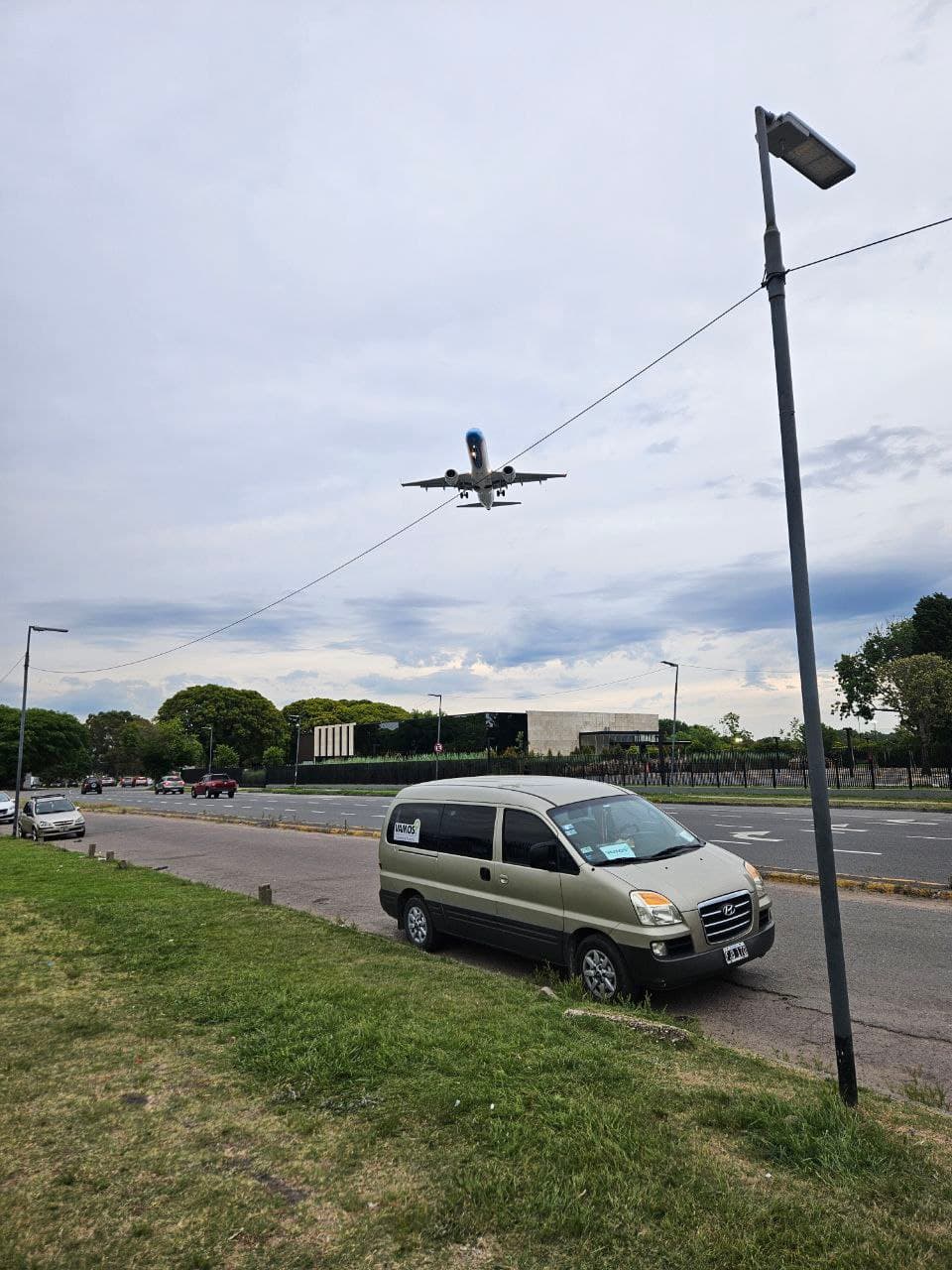 Van de Vamos Traslados estacionada junto a la ruta del aeropuerto mientras aterriza un avión