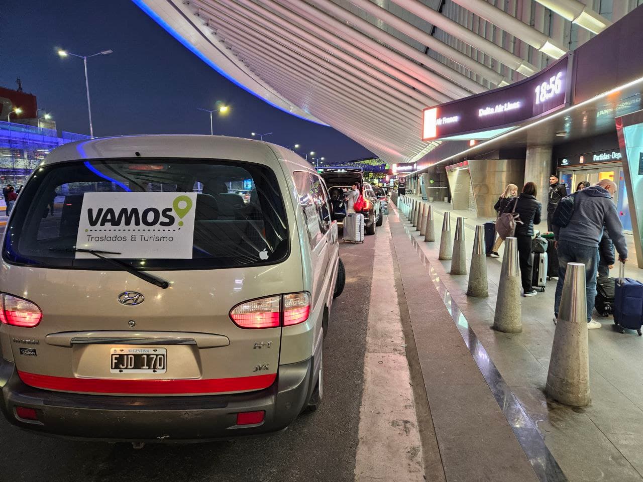 Van de Vamos Traslados & Turismo recibiendo pasajeros con equipaje en el aeropuerto de noche